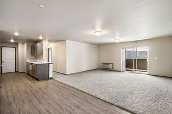 An empty living room with a kitchen and a door to a balcony